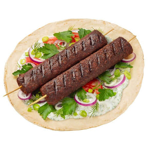 Plant-based kebabs on skewer with flatbread, fresh herbs, onion, tomato, and vegan sauce