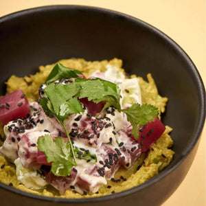 Plant-based poke bowl with creamy dressing, avocado, fresh herbs, and black sesame seeds in a black bowl