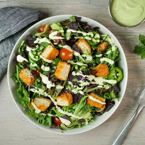 Plant-based chicken salad with mixed greens, cherry tomatoes, and creamy dressing in a bowl