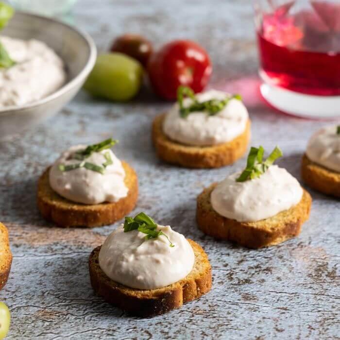 Plant-based crostini with creamy topping and herbs on rustic table, vegan appetizers UAE