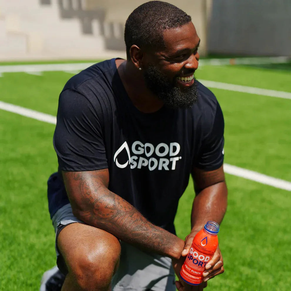 Smiling athlete on sports field holding GoodSport Fruit Punch plant-based drink