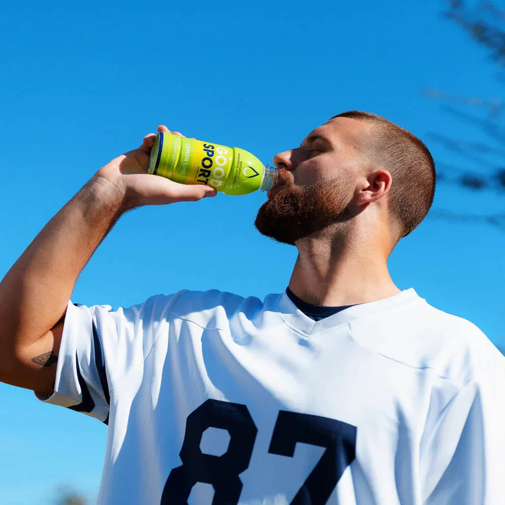 Man in white sports jersey drinking GoodSport Lemon Lime plant-based beverage outdoors