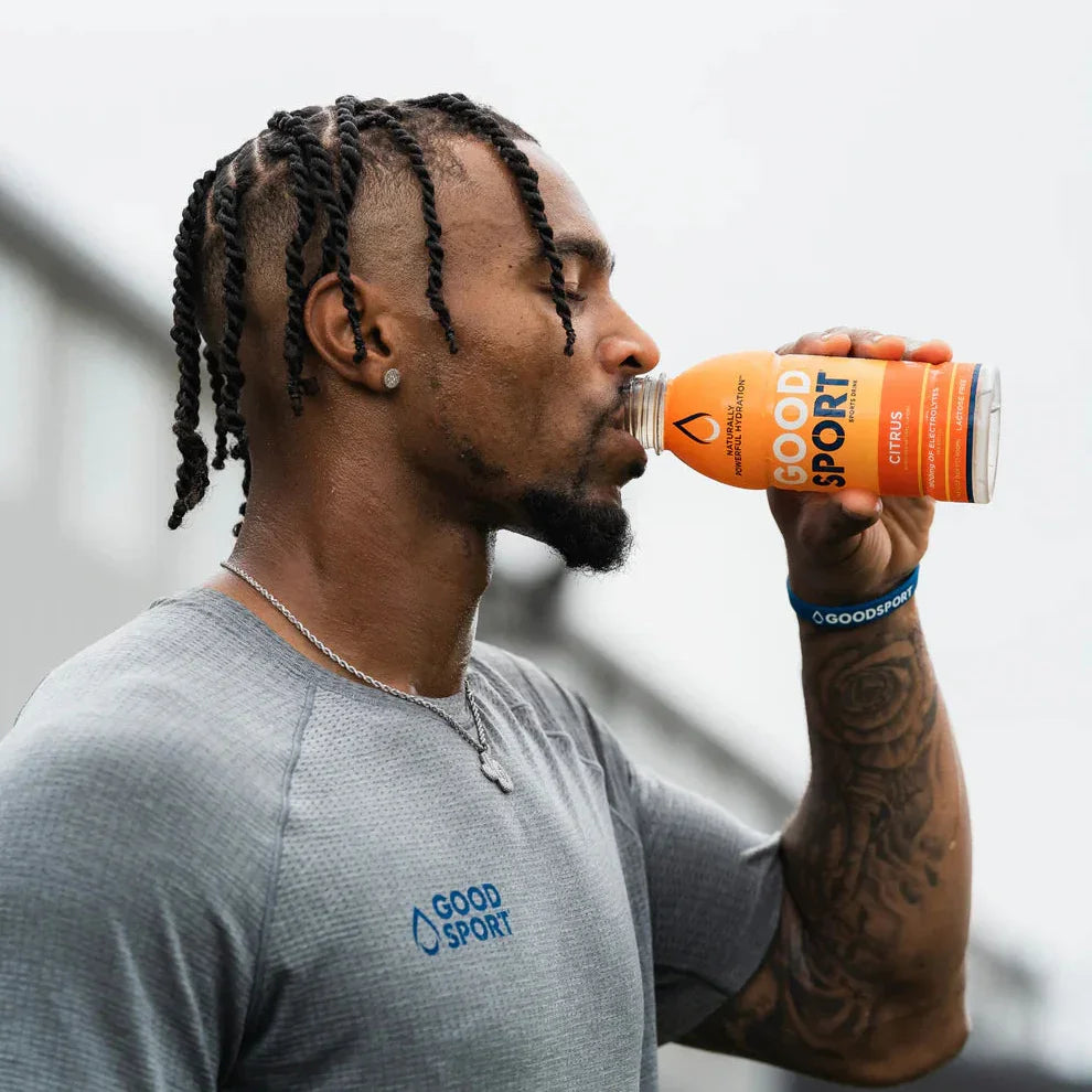 Athlete drinking plant-based GoodSport mango drink, wearing GoodSport shirt, outdoors