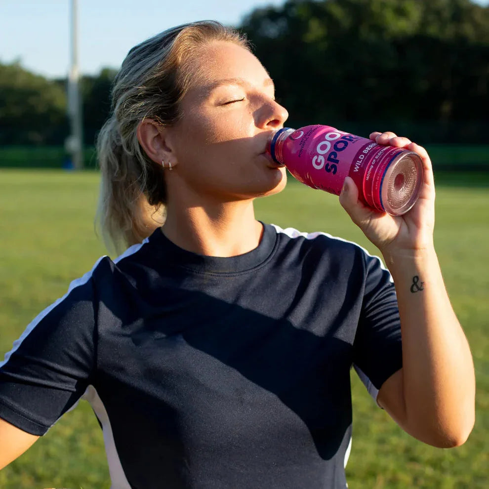 Athlete on soccer field drinking GoodSport Mango drink, holding a ball, plant-based hydration