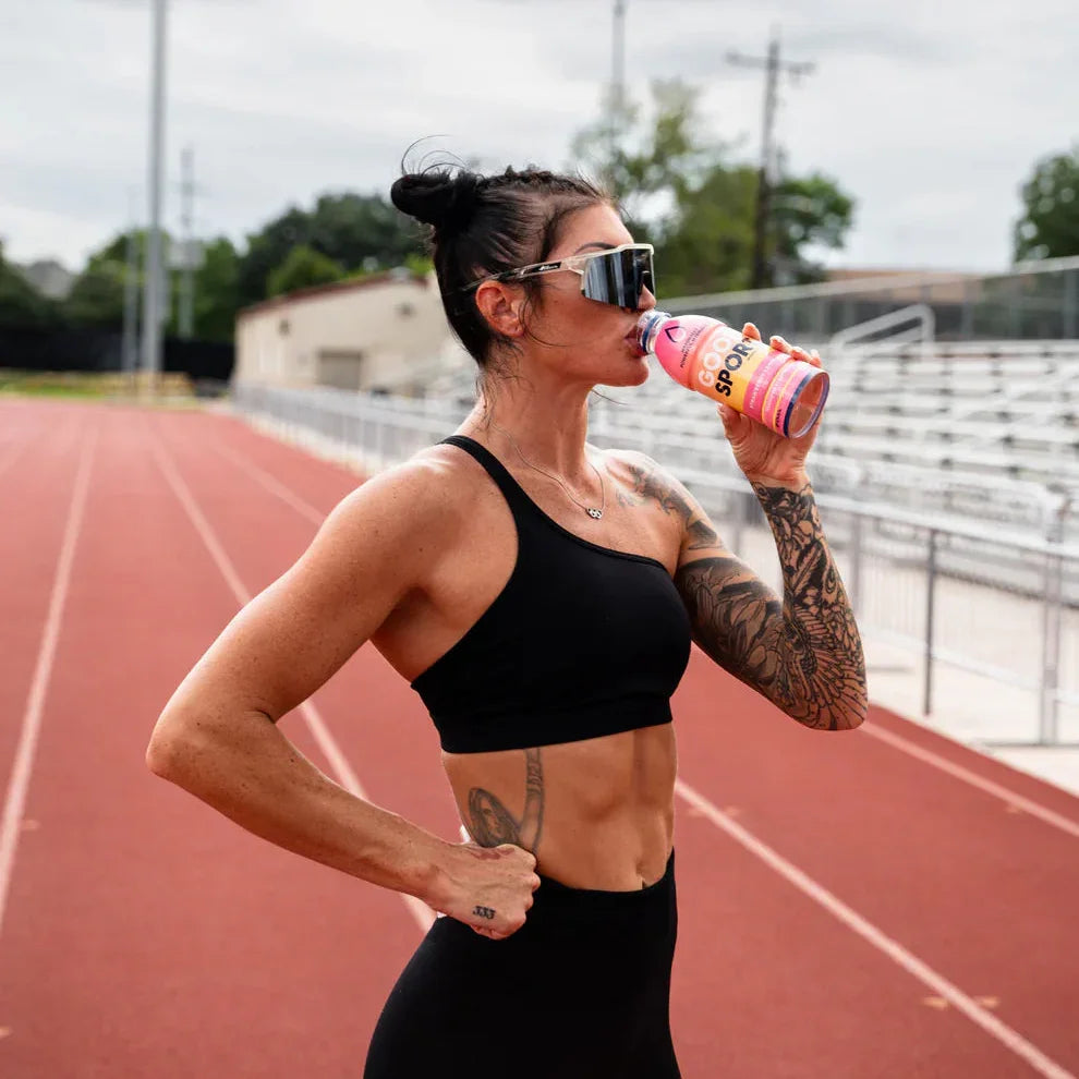 Athletic woman on running track drinking GoodSport Strawberry Lemonade plant-based drink