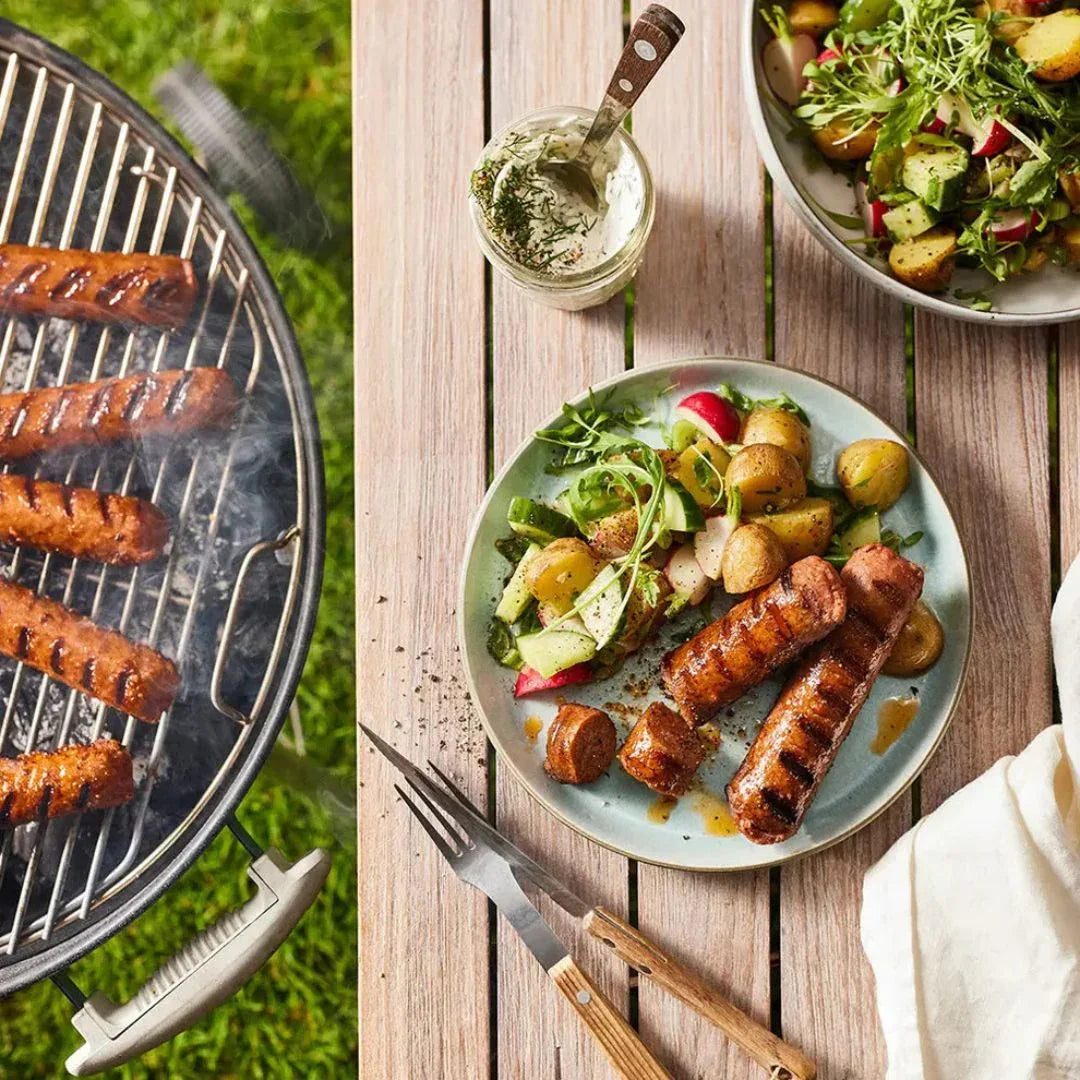 Grilled plant-based sausages on a barbecue and served with potato salad on a wooden table