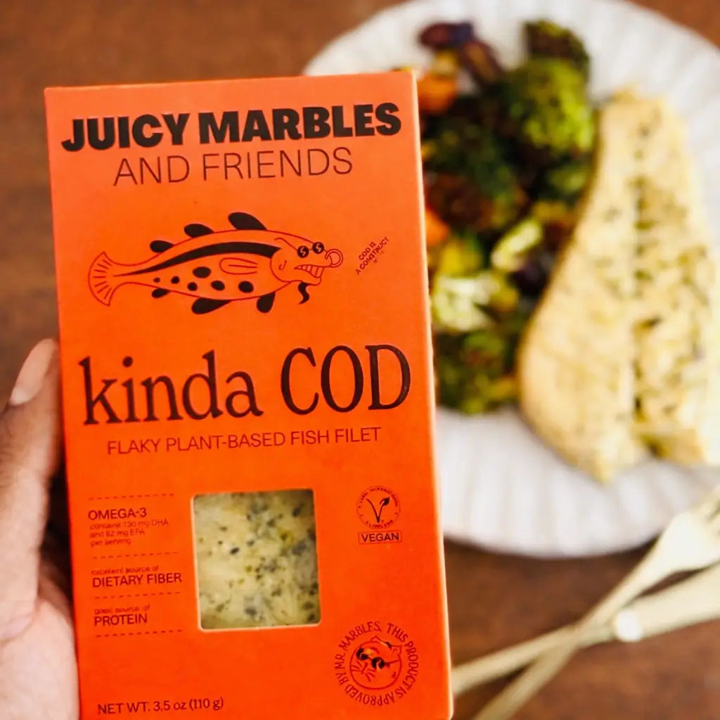 Orange box of 'Juicy Marbles and Friends kinda COD' plant-based fish filet with a blurred background of food.