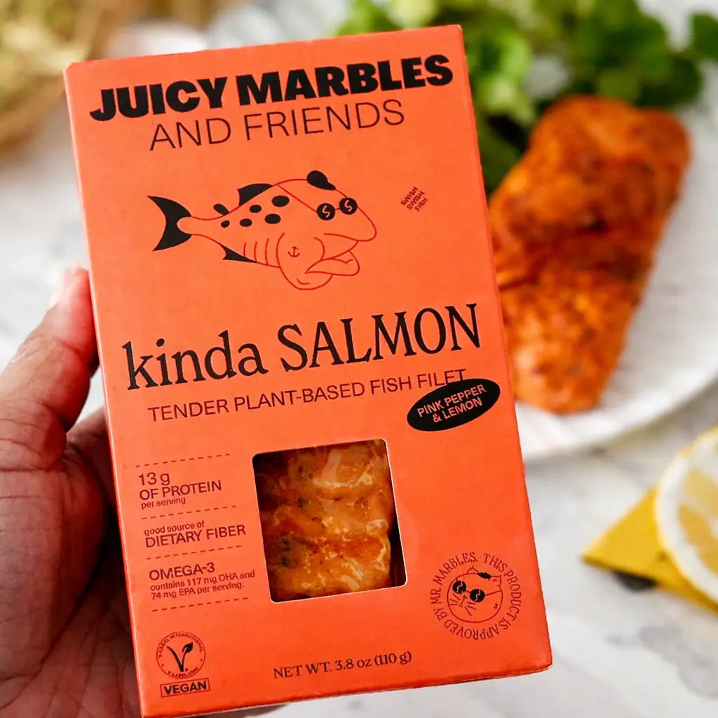 Orange box of 'Juicy Marbles and Friends kinda Salmon' plant-based fish fillets held by a hand.