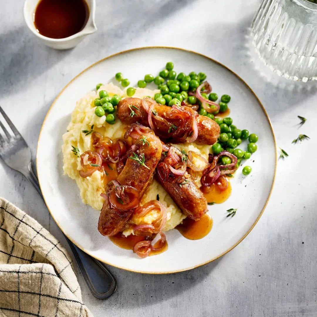 Plant-based sausages with mashed potatoes, gravy, peas, and caramelized onions on plate