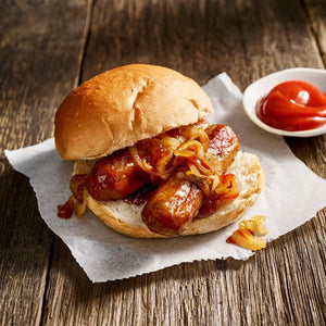Plant-based sausage sandwich with caramelized onions on a bun, served with ketchup, iPlantBased