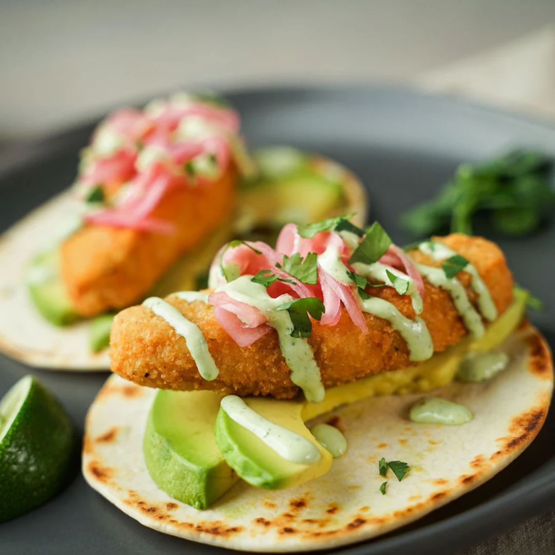 Plant-based tacos with breaded filling, avocado, pickled onions, and creamy sauce on tortillas