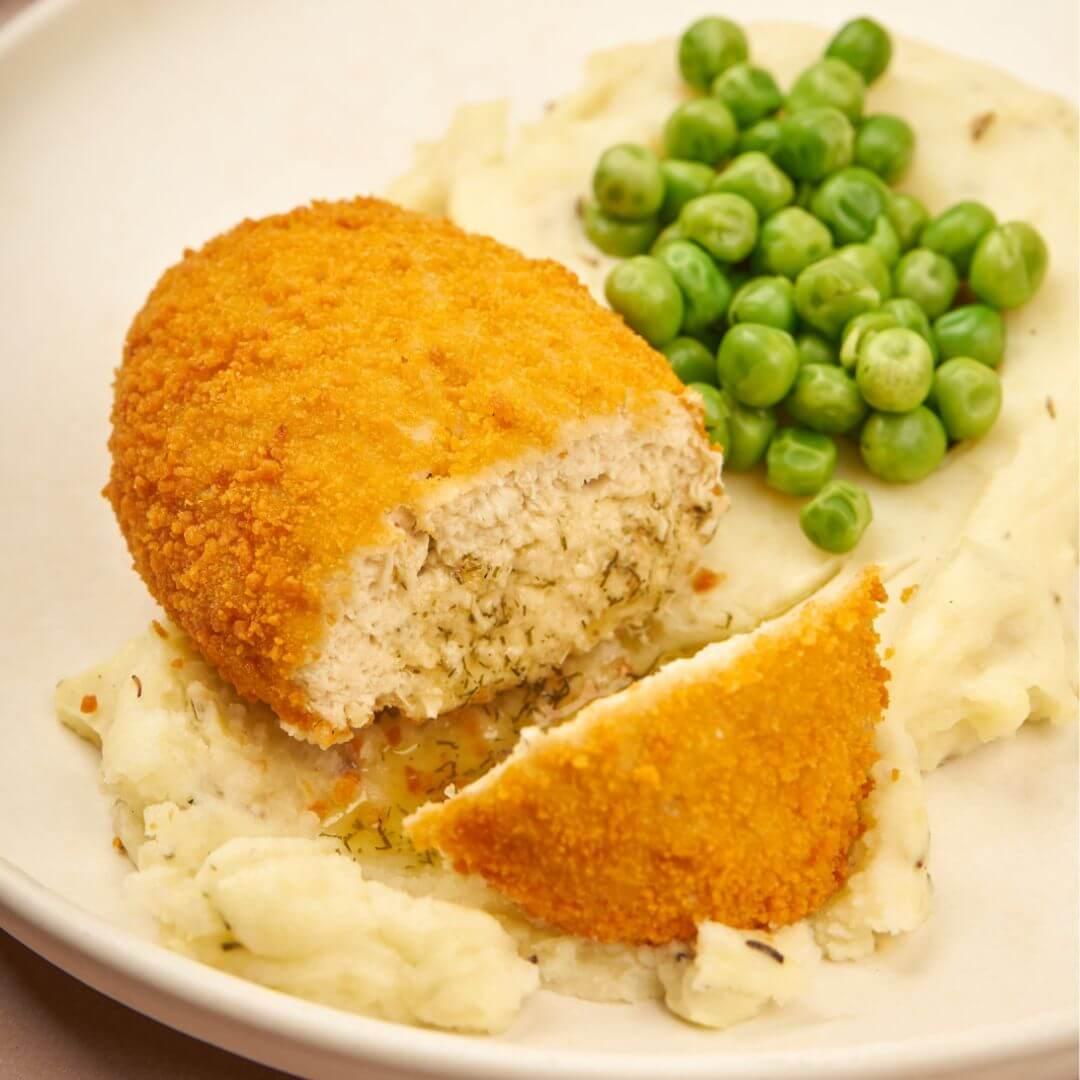 Plant-based breaded cutlet with mashed potatoes and peas on white plate