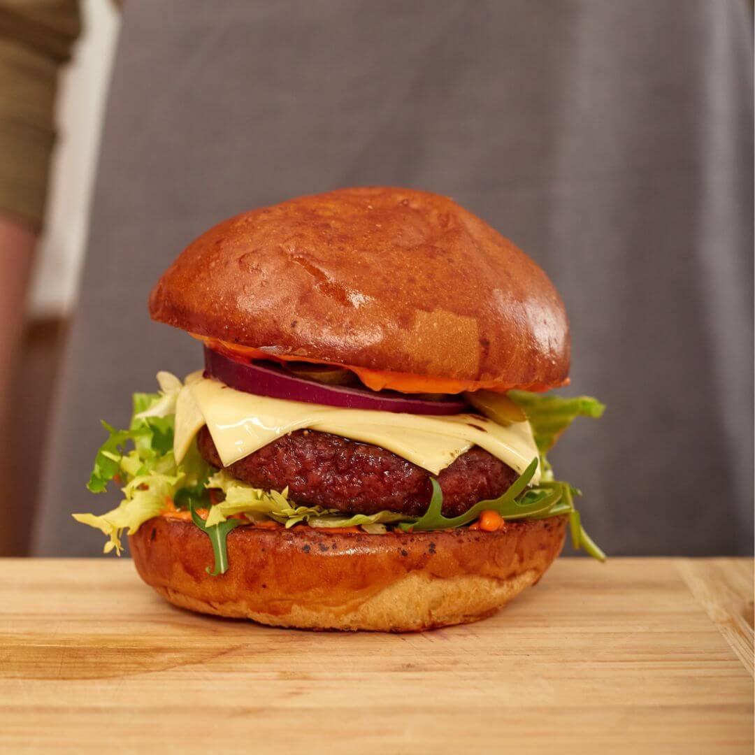 Plant-based burger with lettuce, vegan cheese and onions on a wooden board at iPlantBased UAE