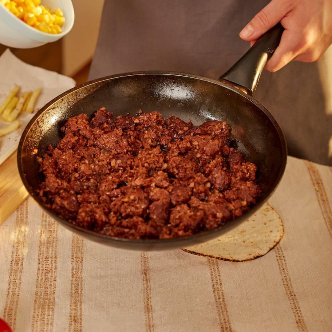 Plant-based meat cooking in skillet, iPlantBased vegan food UAE, tortilla and corn nearby