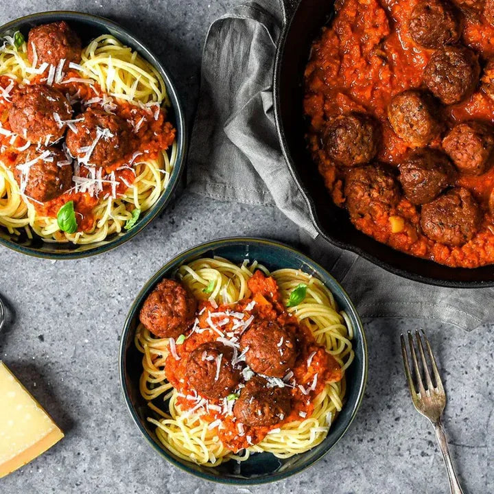 Plant-based meatballs with tomato sauce over spaghetti, garnished with fresh basil and vegan cheese