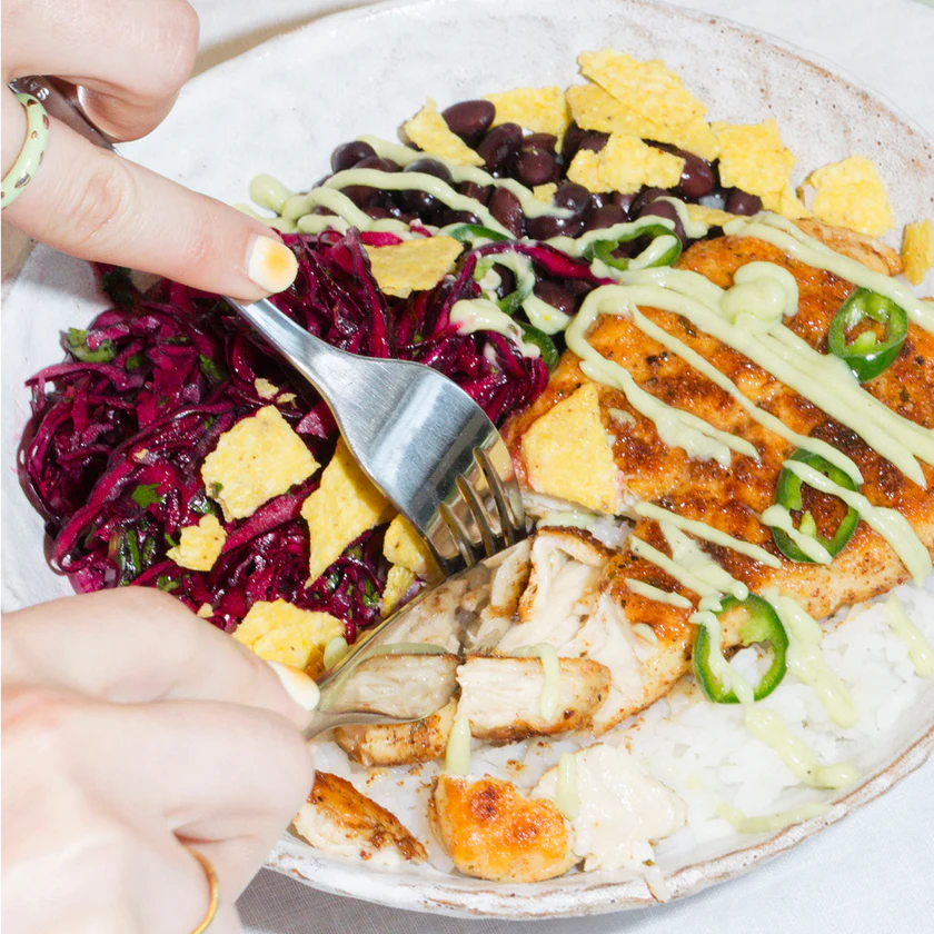 Plated dish with salmon, vegetables, and a creamy sauce being cut into with a fork.