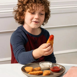 Child enjoying plant-based nuggets with ketchup and dip at iPlantBased food store.