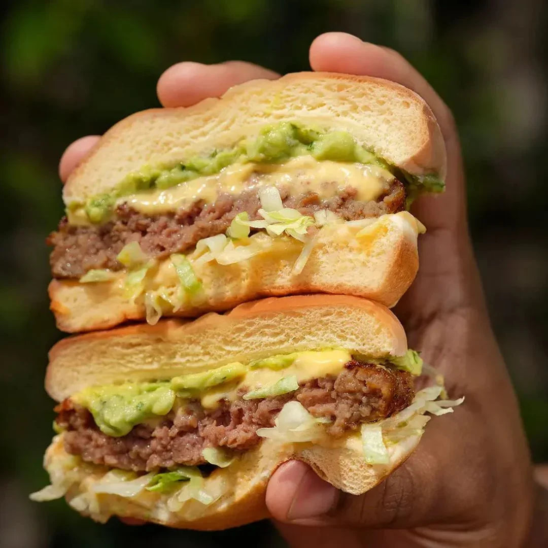 Hand holding a plant-based burger with lettuce, avocado, and sauce from iPlantBased UAE