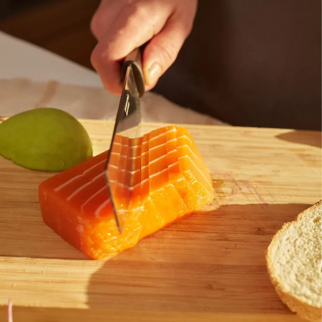 Hand slicing plant-based salmon sashimi on wooden board with bread and avocado, iPlantBased UAE
